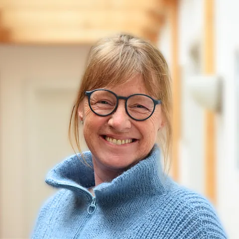 Lächelnde Frau mit Brille und blauem Pullover.