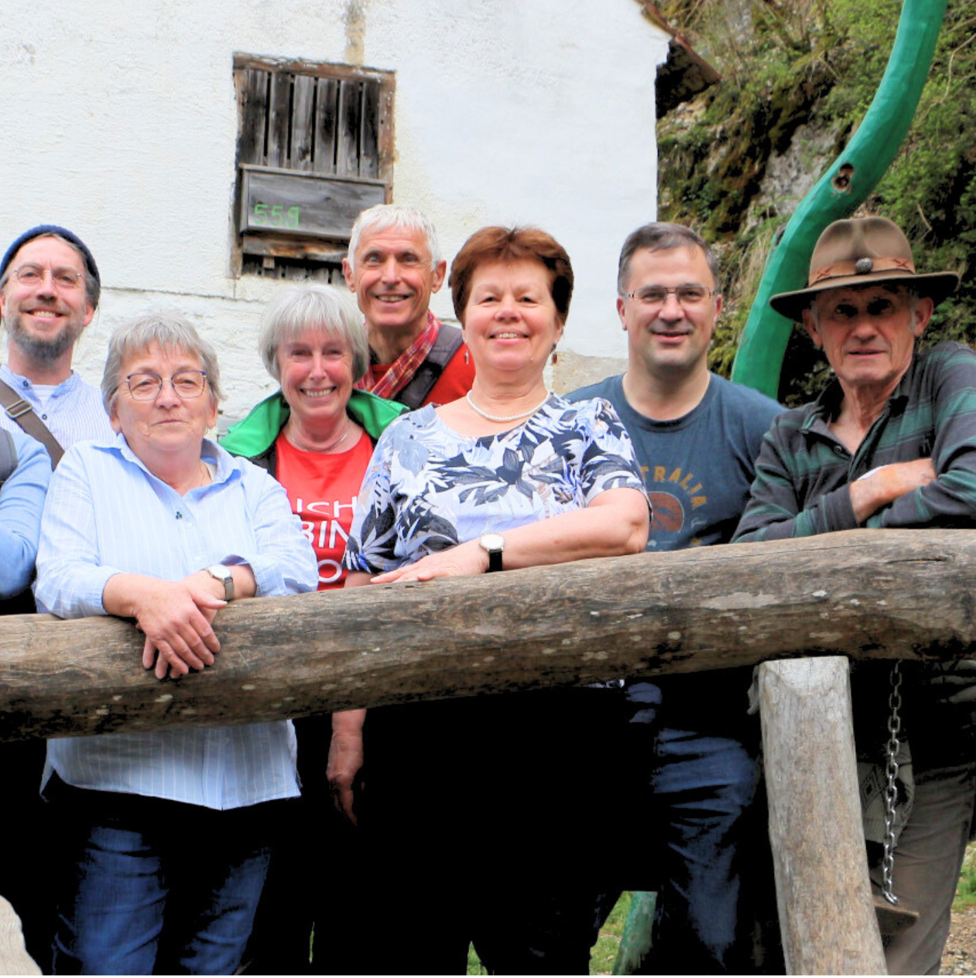 Eine Gruppe lächelnder Menschen posiert draußen an einem Holzzaun.