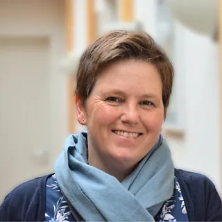 Lächelnde Frau mit kurzen braunen Haaren und blauem Schal.
