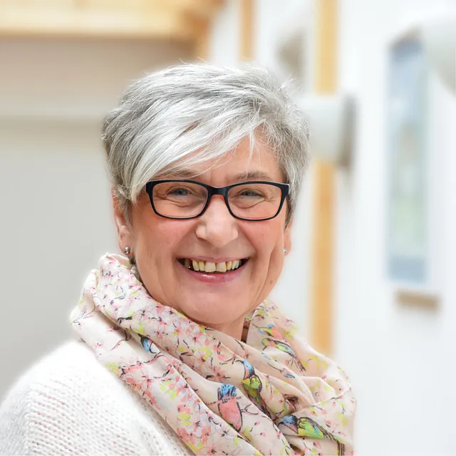 Lächelnde Frau mit Brille und kurzen grauen Haaren.