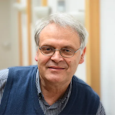 Lächelnder Mann mit Brille und blauer Weste.