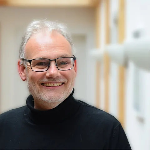 Lächelnder Mann mit Brille und schwarzem Pullover.