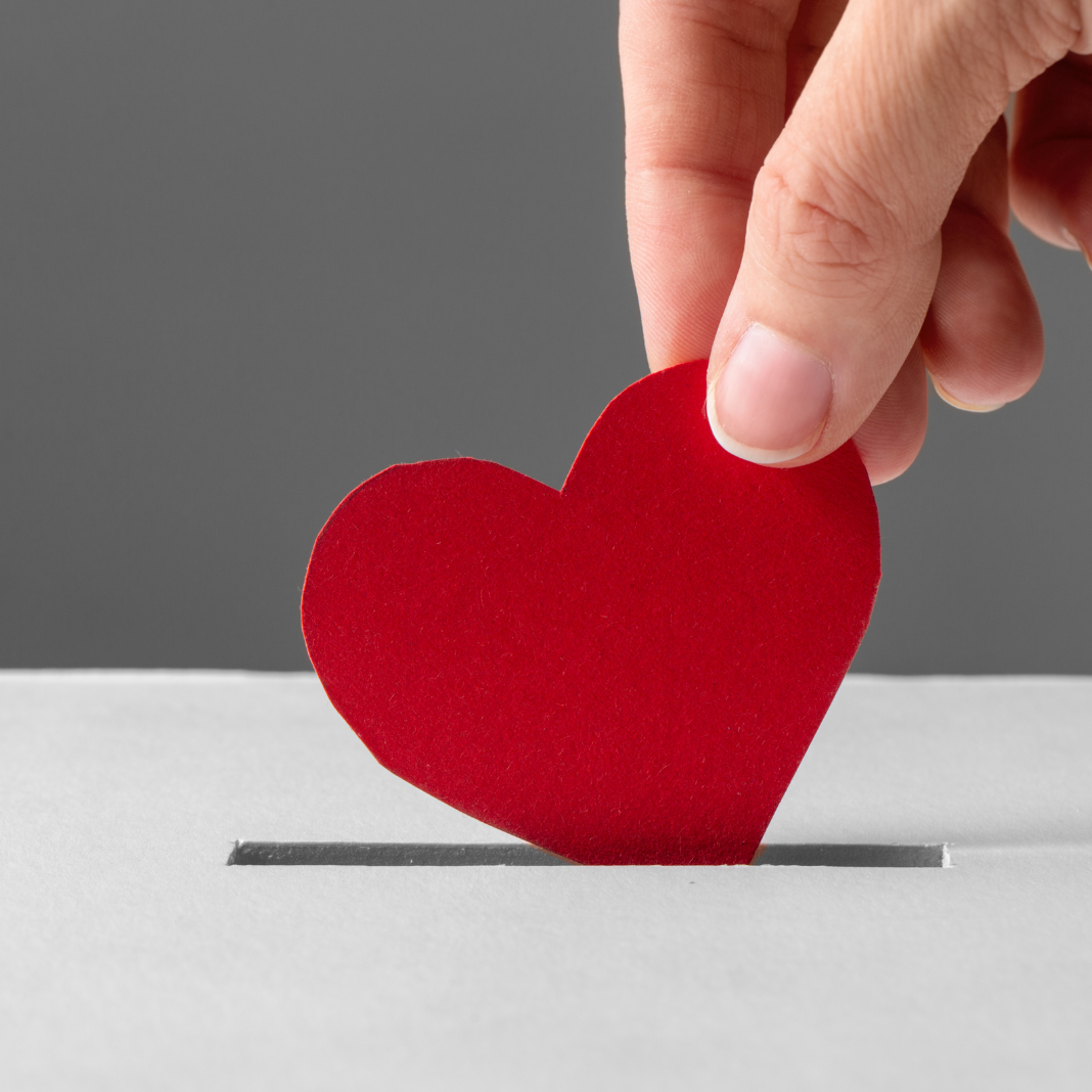 Hand legt rote Herzkarten in den Schlitz, symbolisiert Liebe oder Spende.