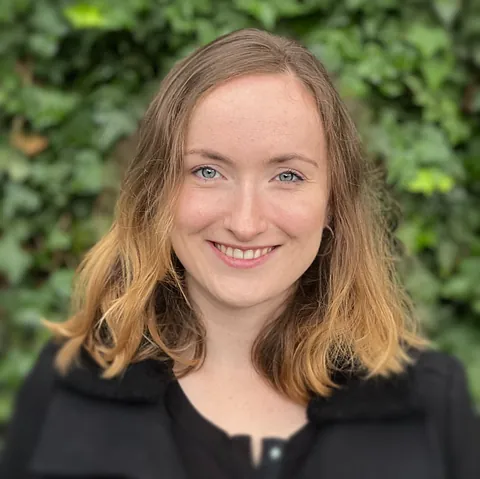 Lächelnde Frau mit blondem Haar und schwarzem Mantel.