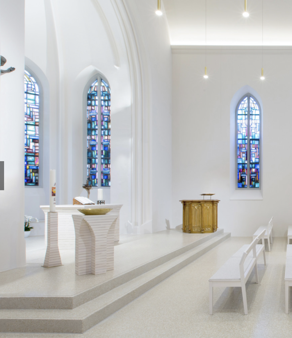 Moderner Kircheninnenraum mit Altar, Kanzel, Buntglasfenstern und weißen Bänken.