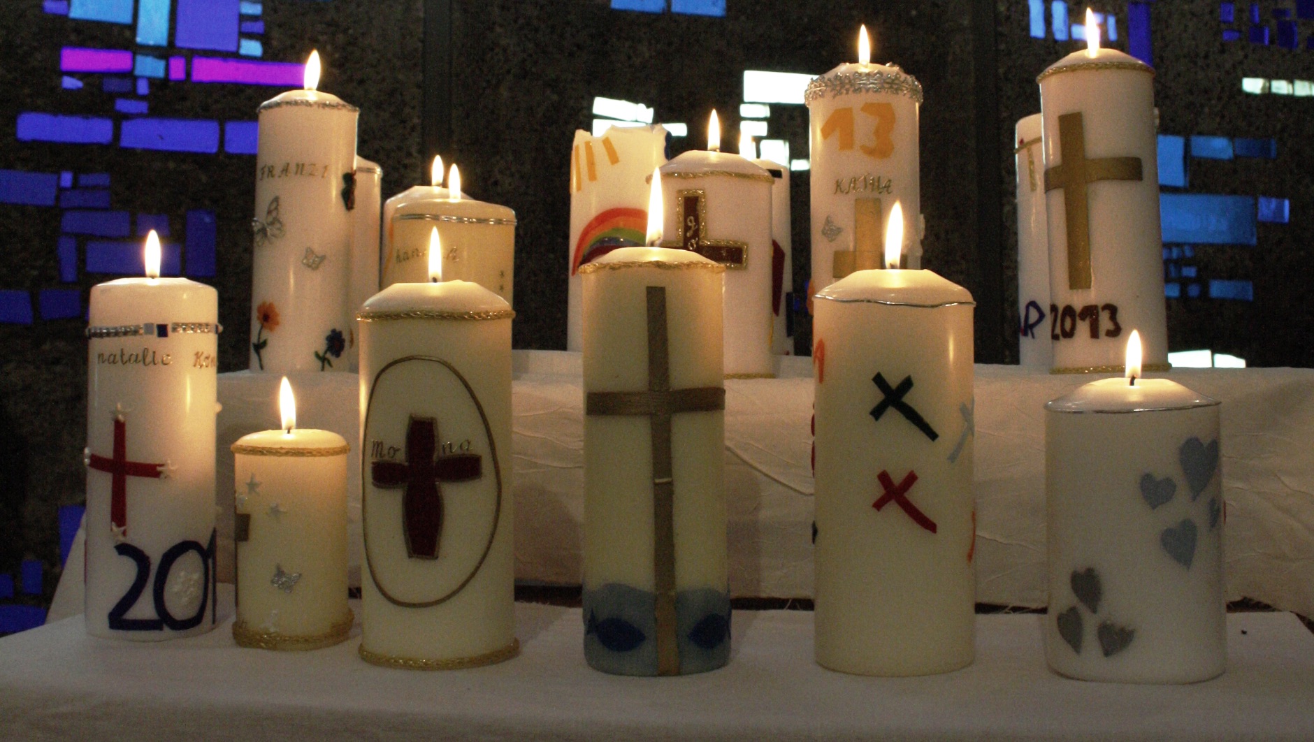 Brennende Konfirmationskerzen mit christlichen Symbolen in einer Kirche.