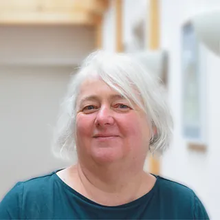 Frau mit kurzen weißen Haaren, die ein petrolfarbenes Shirt trägt und leicht lächelt.